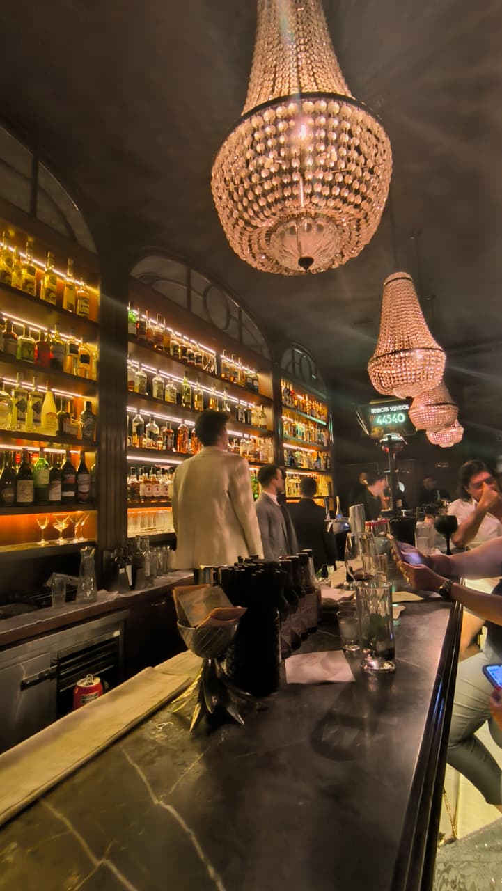 Barra de bar con arañas de cristal y estanterías iluminadas de botellas